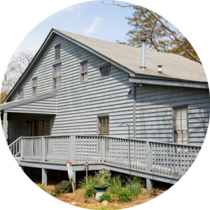Circle Photo: the outside of a house with grey siding. The focus of the photo is the accessible ramp running along the side of the house.